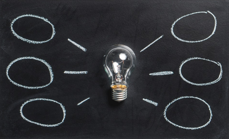 Light bulb on a black background with 3 lines drawn in white either side of the bulb that connect to a circle also drawn in white.