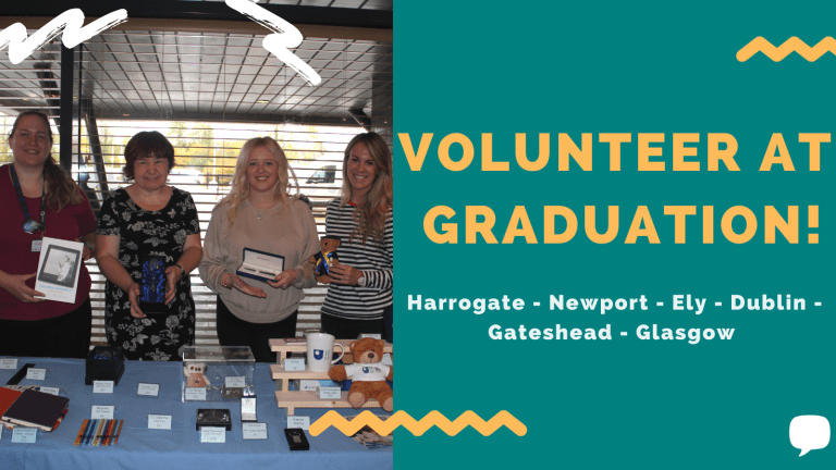 4 people stood behind a table displaying Open University merchandise, with a green block on the right that has yellow text saying 'Volunteer as graduation!' with a list of graduation locations underneath.