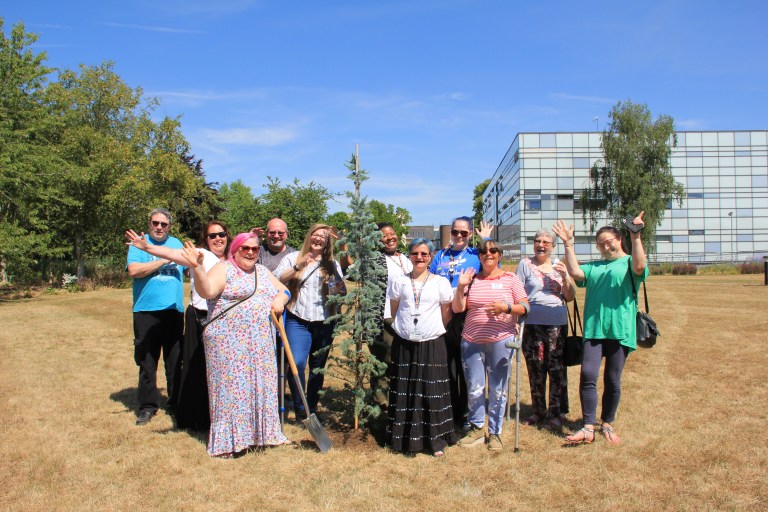 A group of people stood outside together, looking at the camera and waving happily.