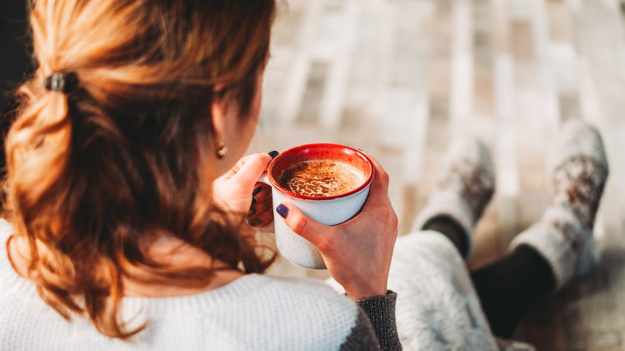 A person holding a mug with a hot drink in it.