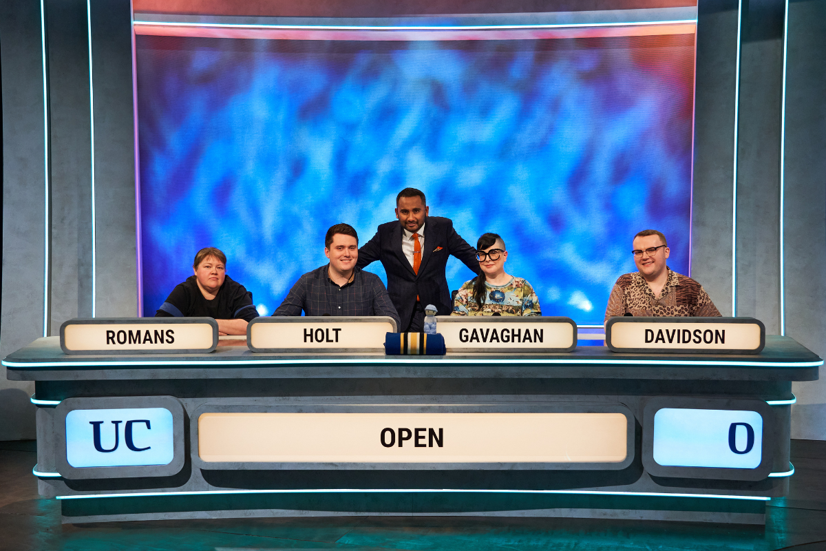 A photo of the OU University Challenge team on the set of the show, with Amol Rajan (the host) stood in the middle of the team.