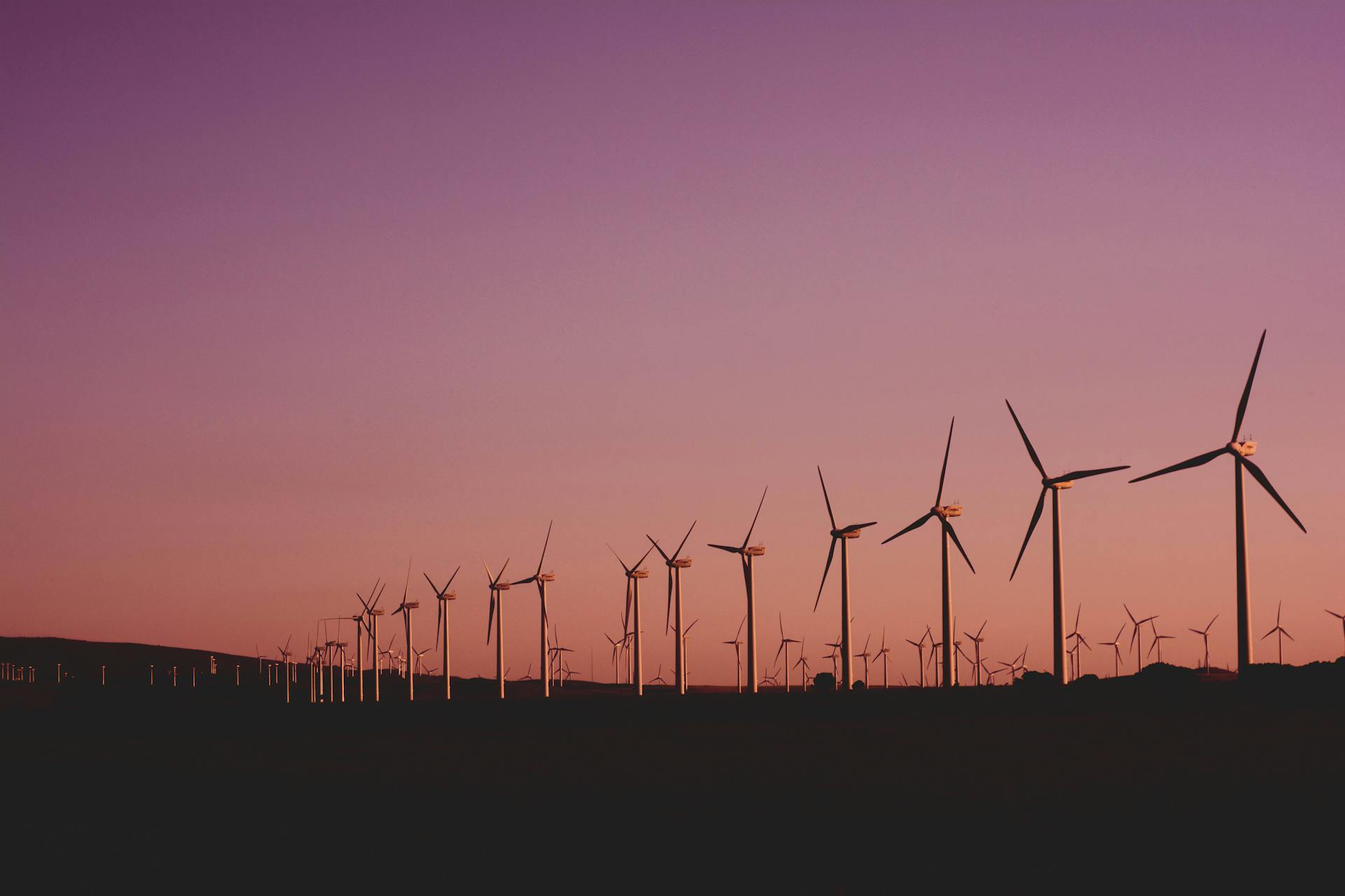 A line of wind turbines against a sunset sky.