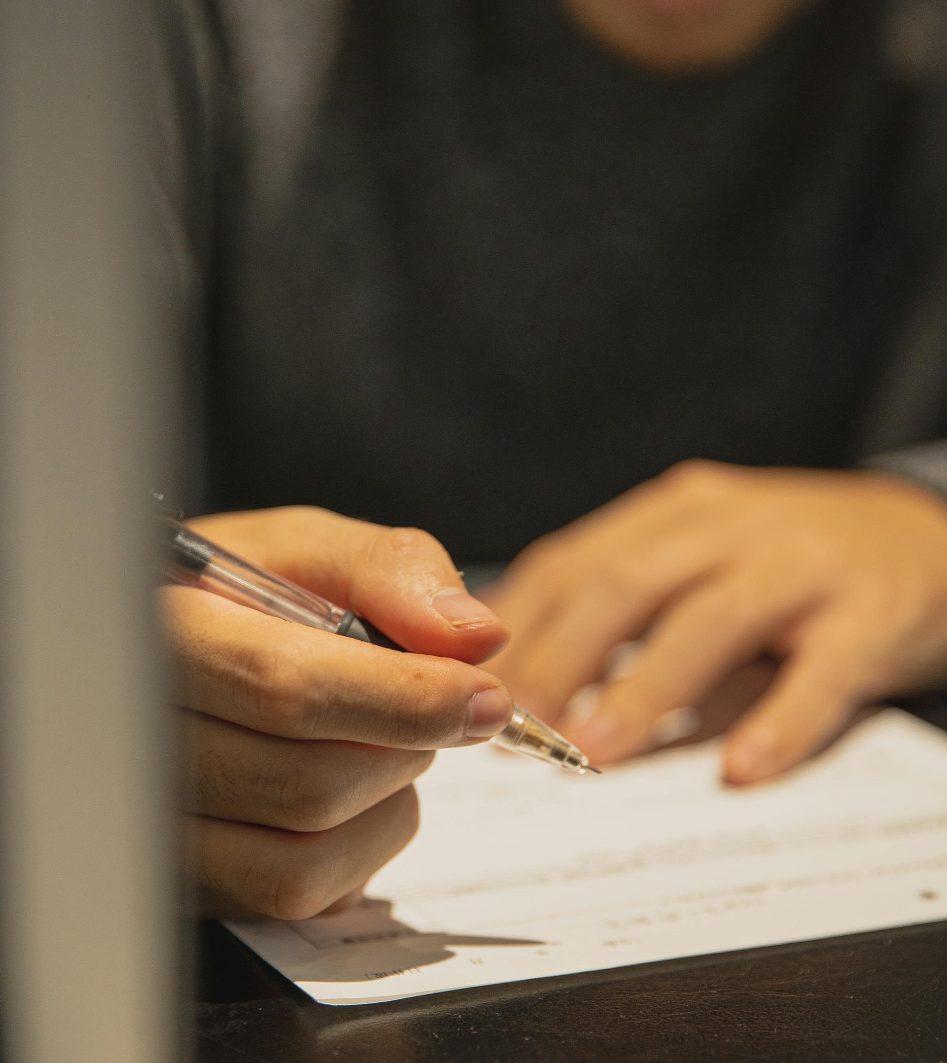 Someone writing on a piece of paper. The focus of the photo is on the person's hands.