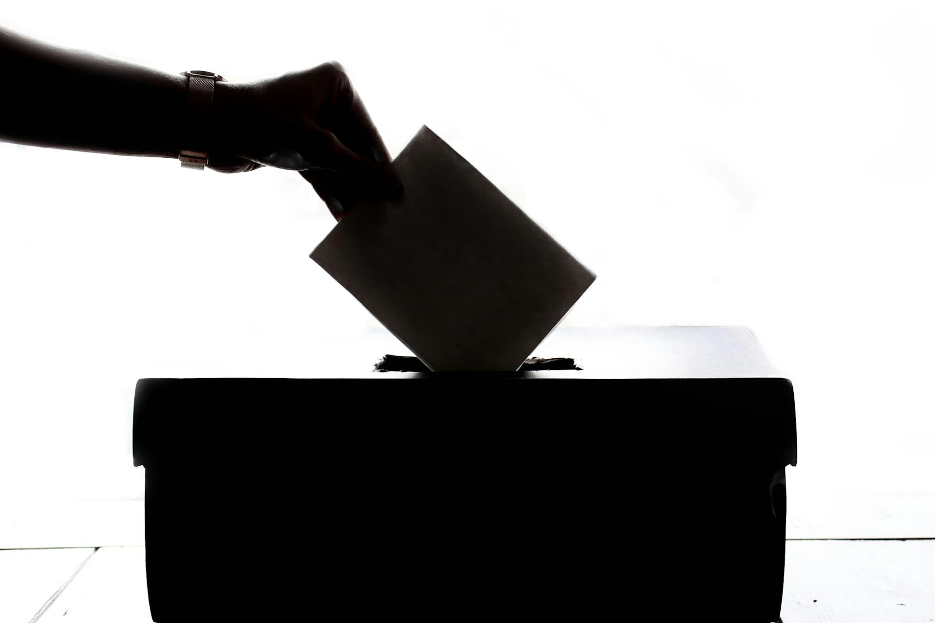 A silhouette of a hand putting a vote into a ballot box.