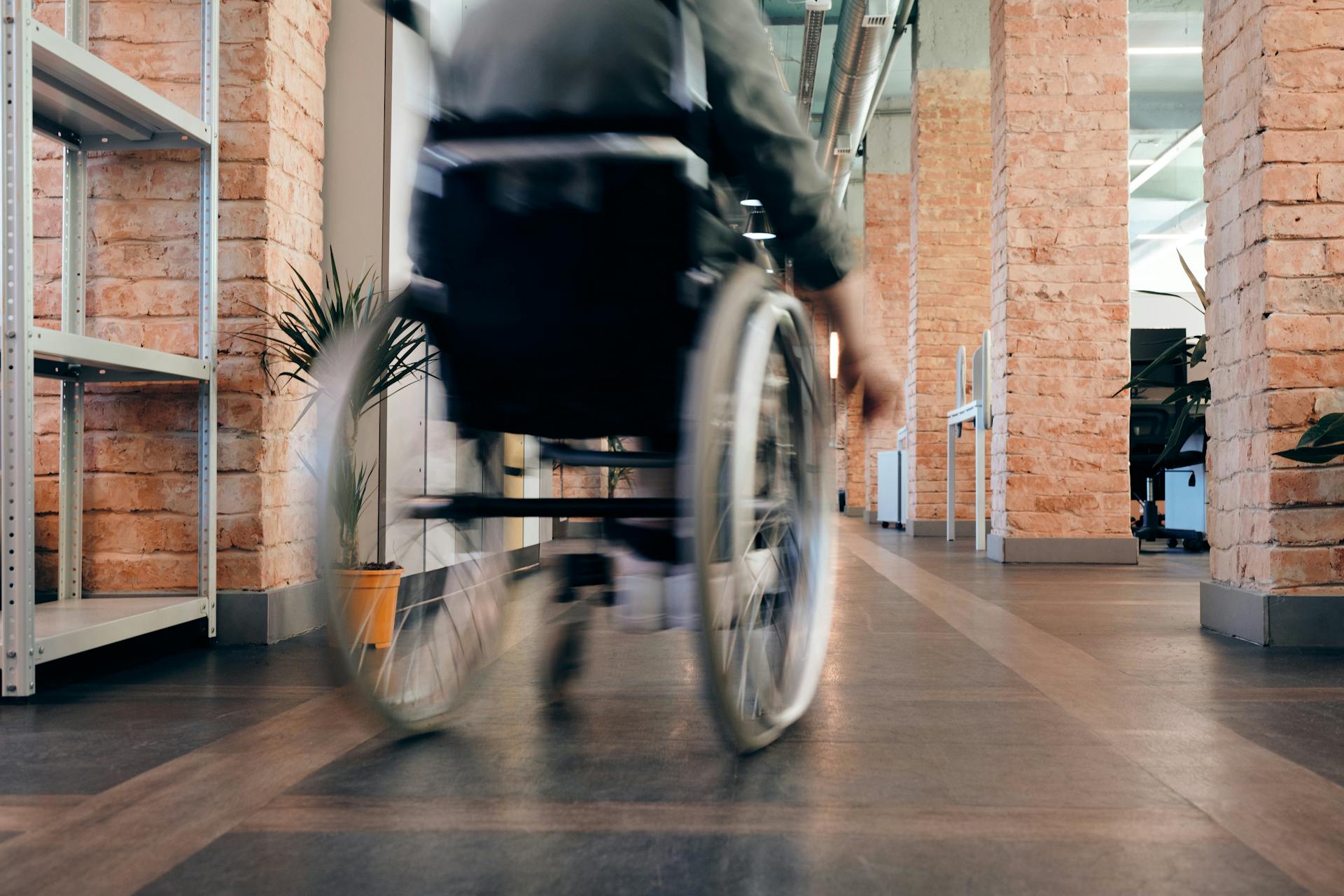 A slightly blurred image of a person in a wheelchair in a corridor. They have their back to the camera.
