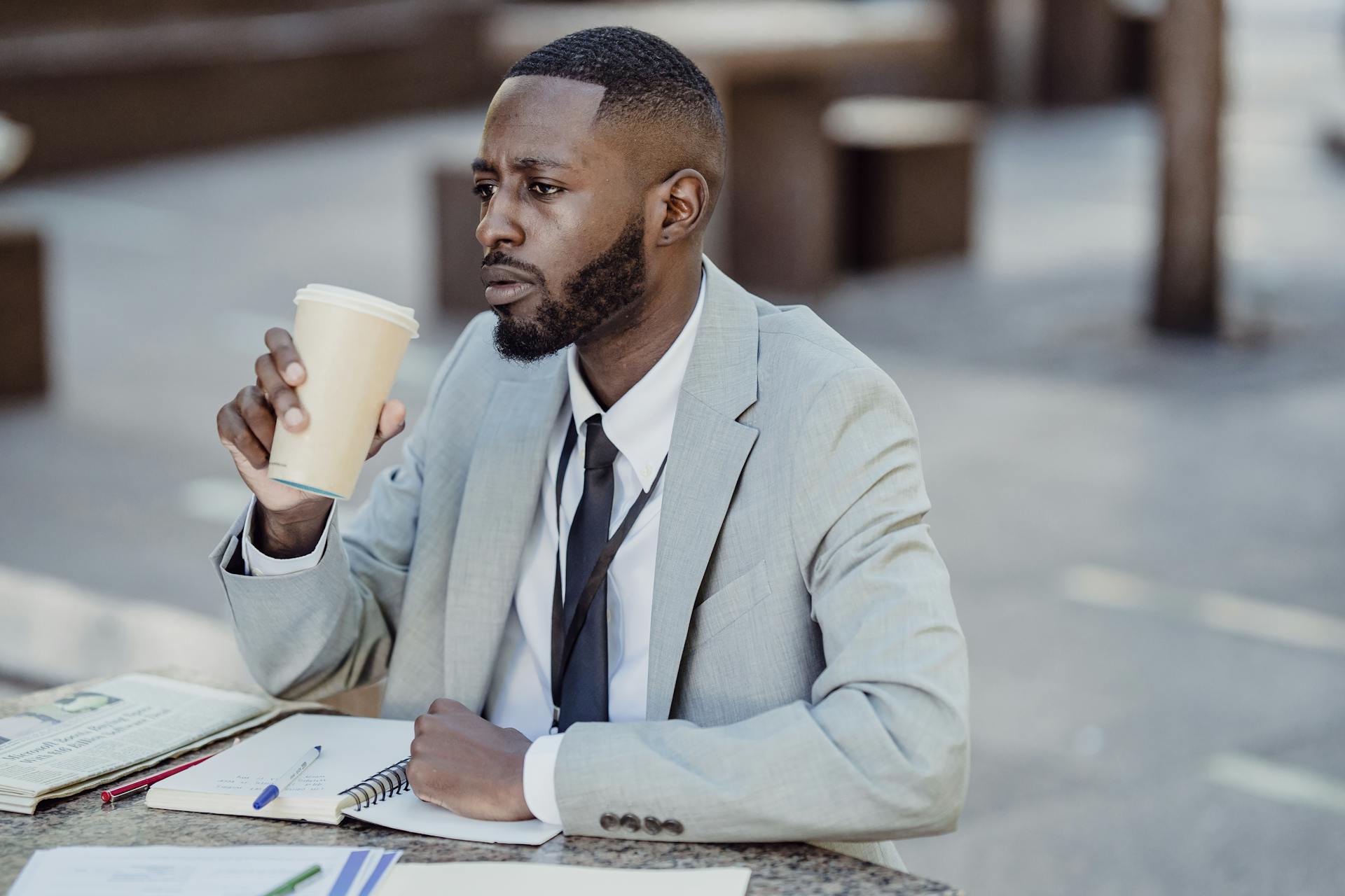A man sat at a desk, drinking coffee and looking into the distance.