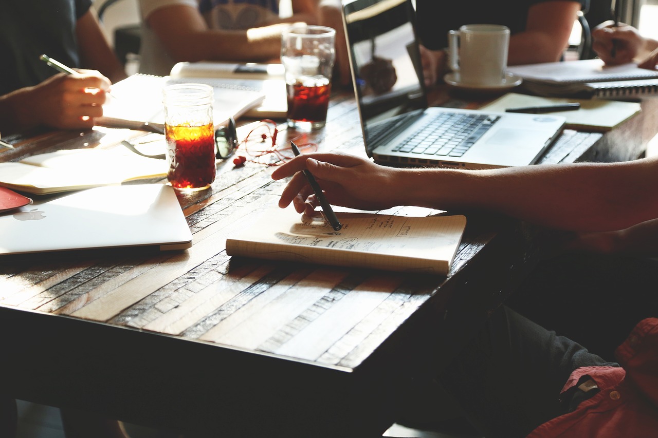 Close up of a table with several people around it working on laptops or writing in notepads.