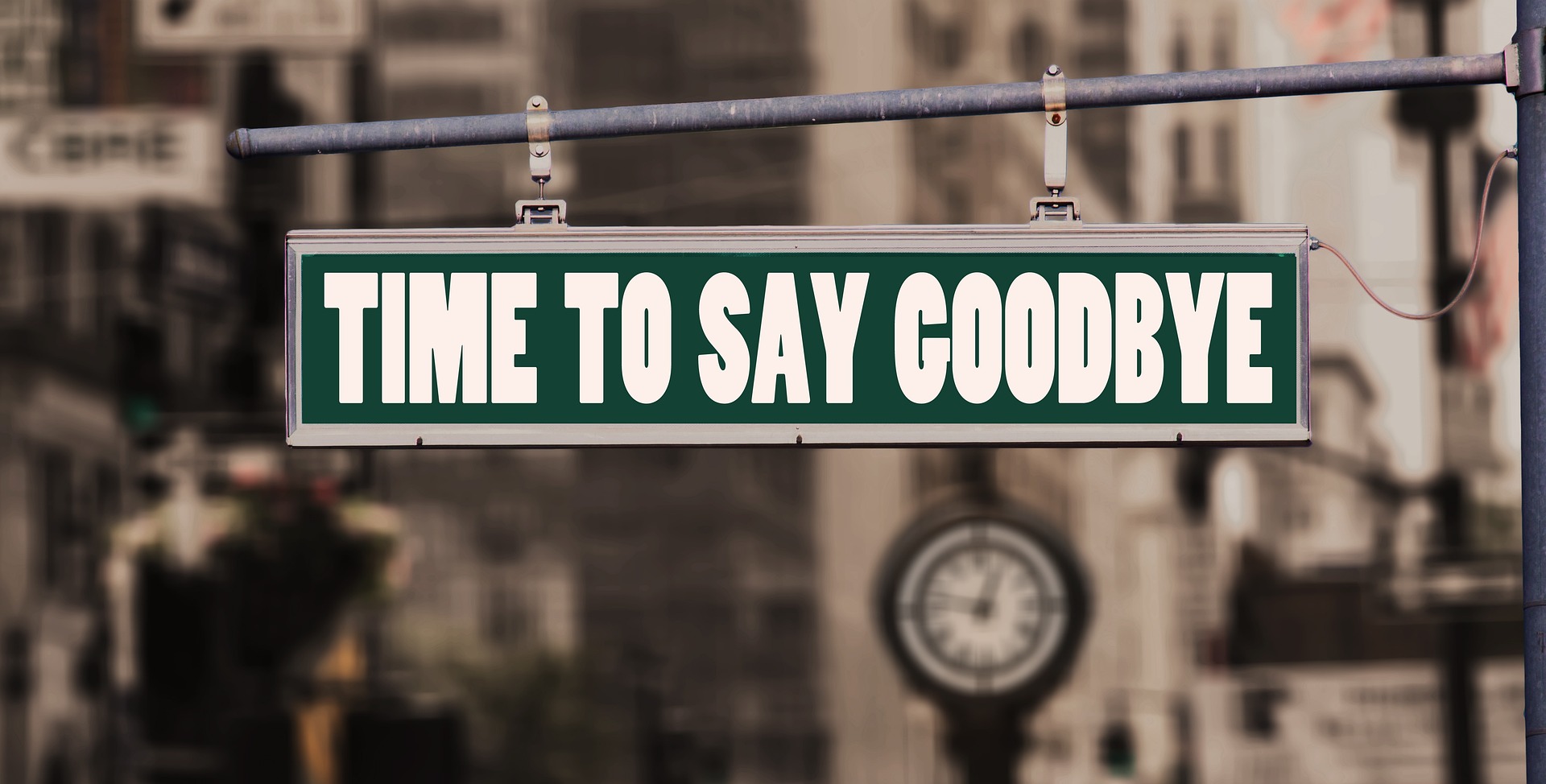 A green sign across a street which says 'Time to say goodbye'.