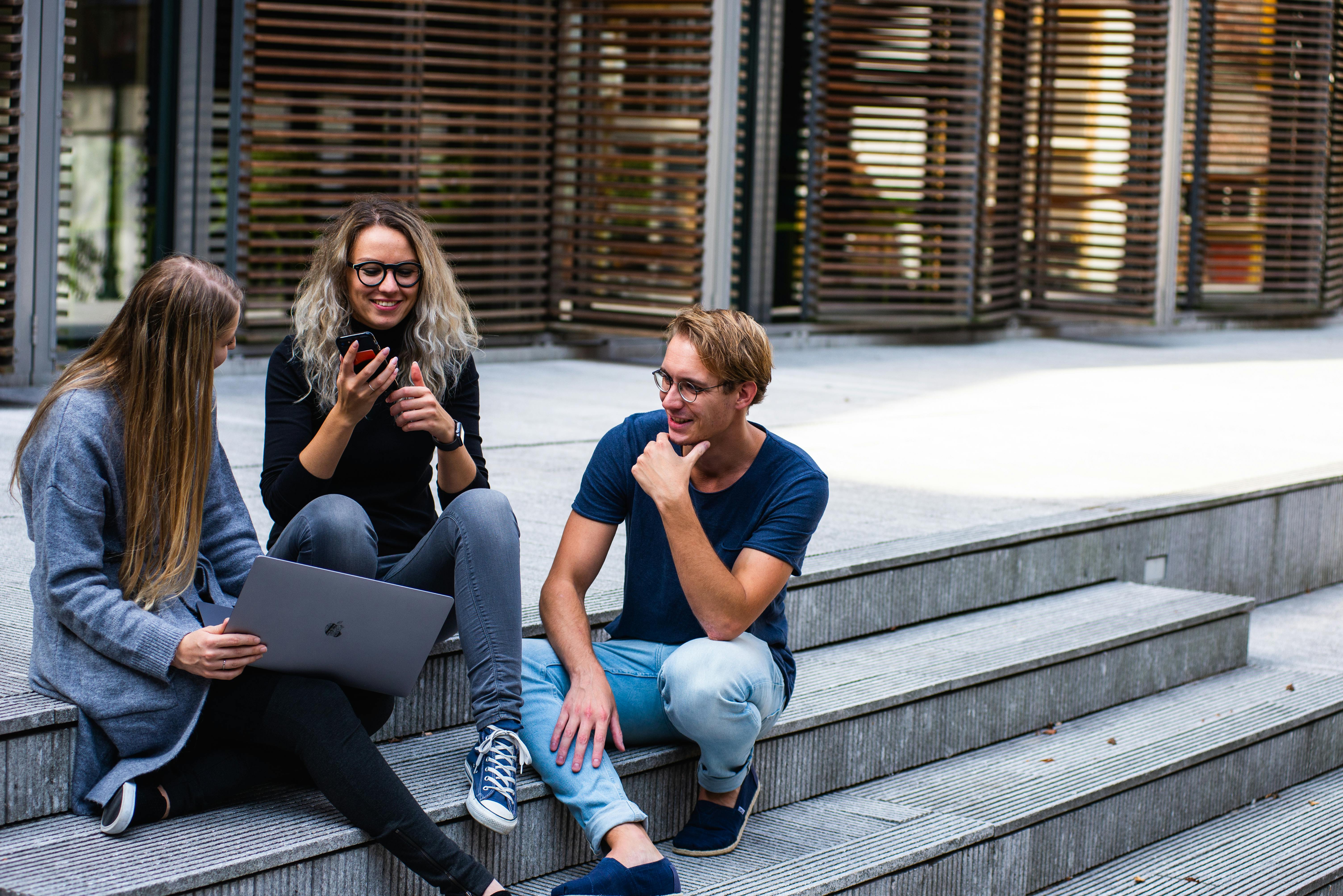 Three people sat outside on some steps, chatting and smiling.
