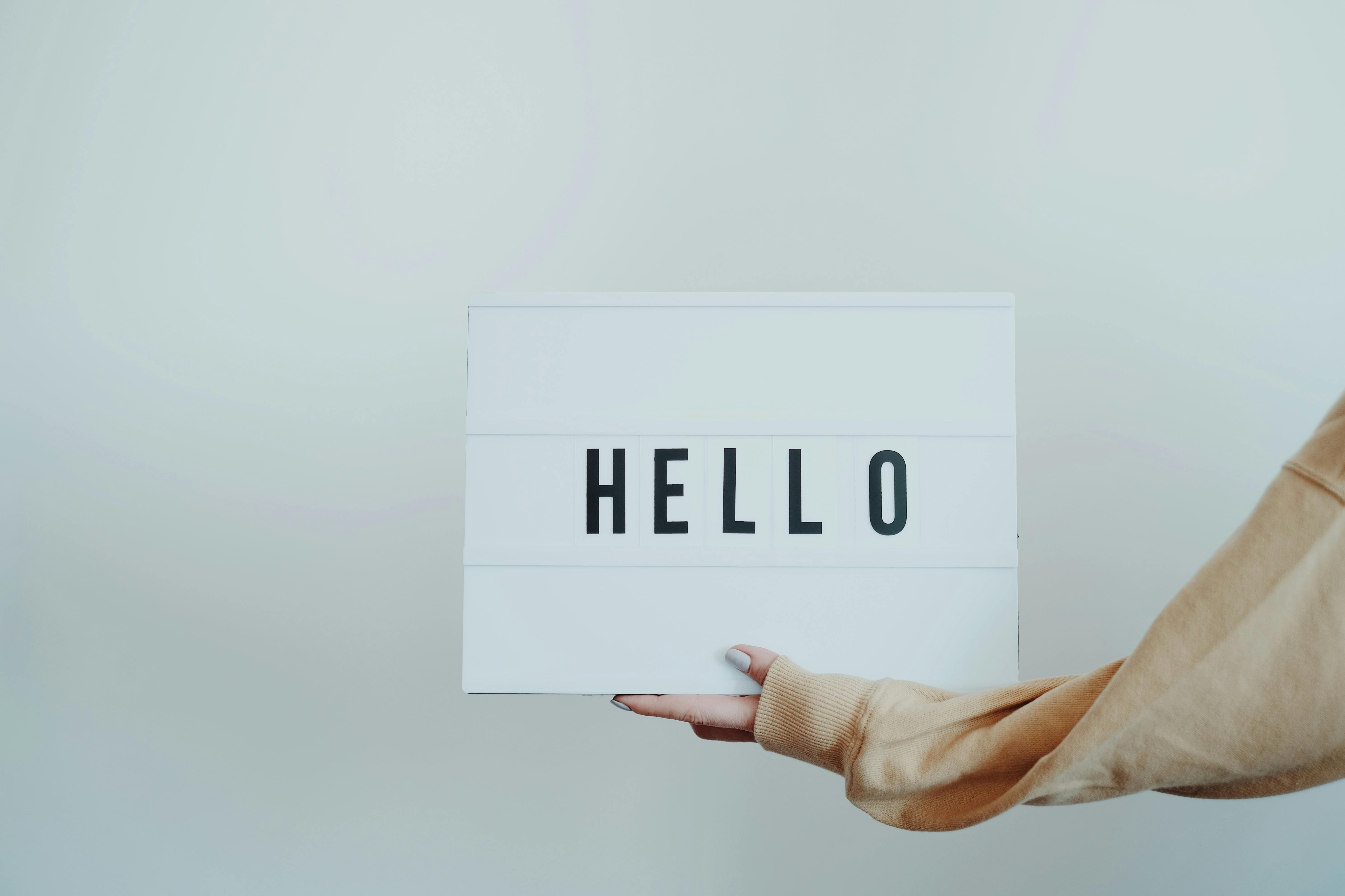 An arm coming into the photo, holding a sign which says 'Hello'.