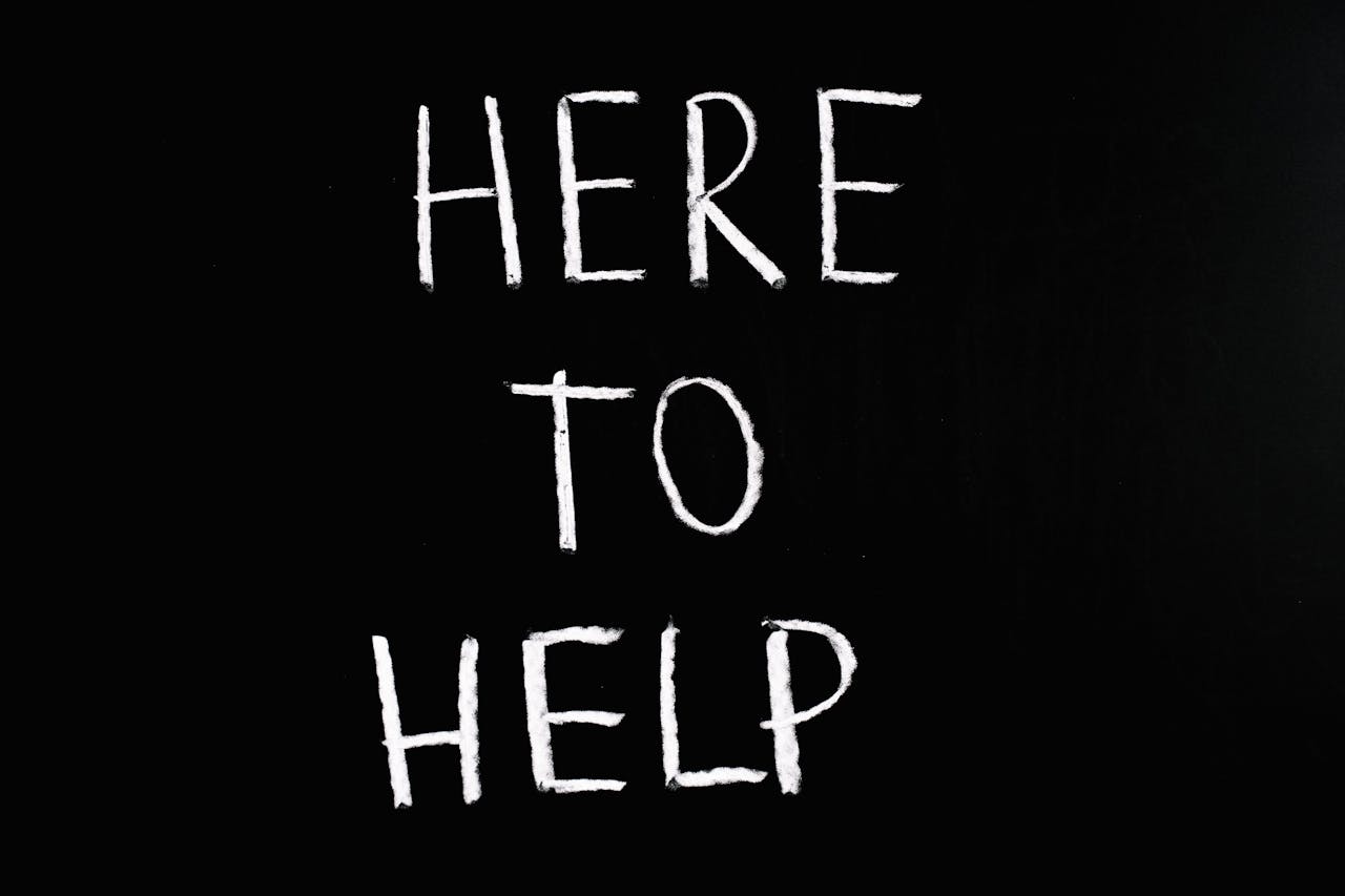 The phrase 'Here to help' written in chalk-type writing on a black background.