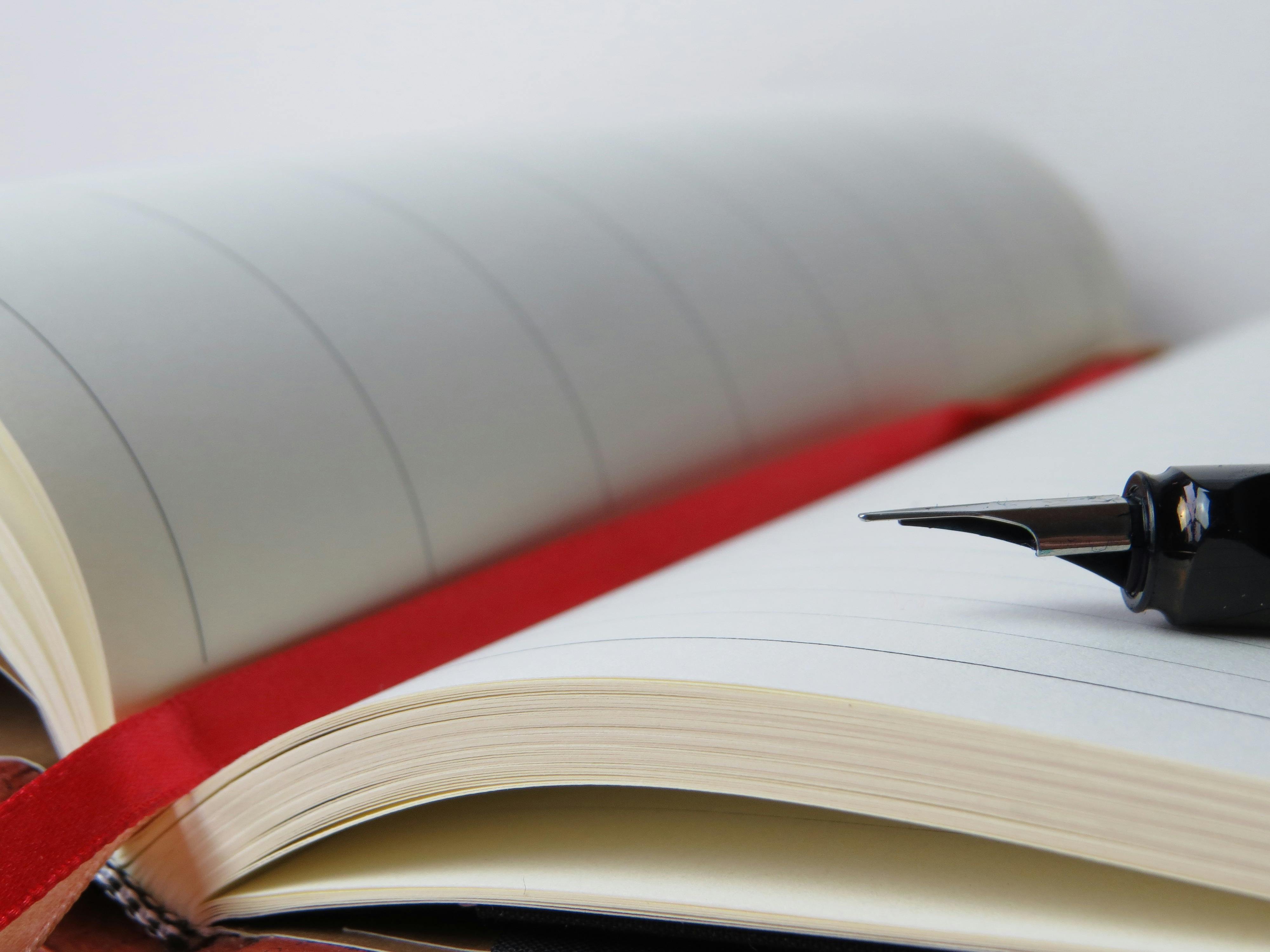 An open book with a red margin and a pen resting on the right-hand page.