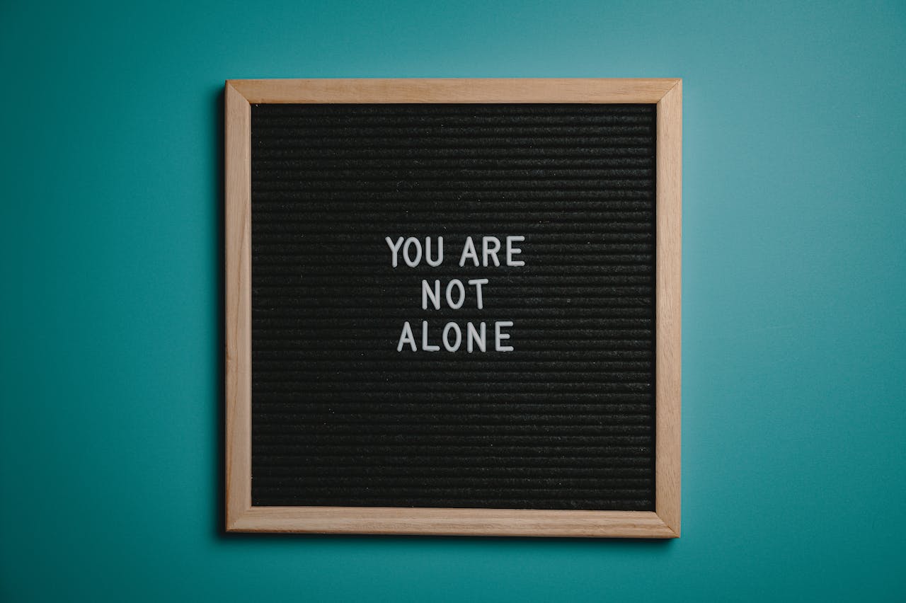 A blackboard with a sign saying 'You are not alone'. The background behind the blackboard is turquoise.
