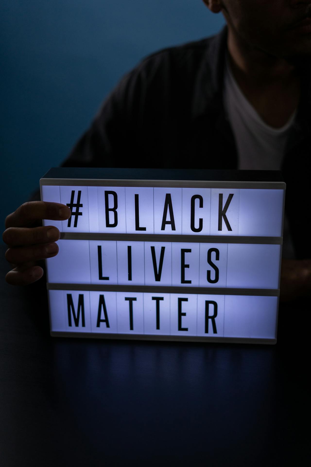Someone holding up an illuminated sign saying '# Black Lives Matter'.