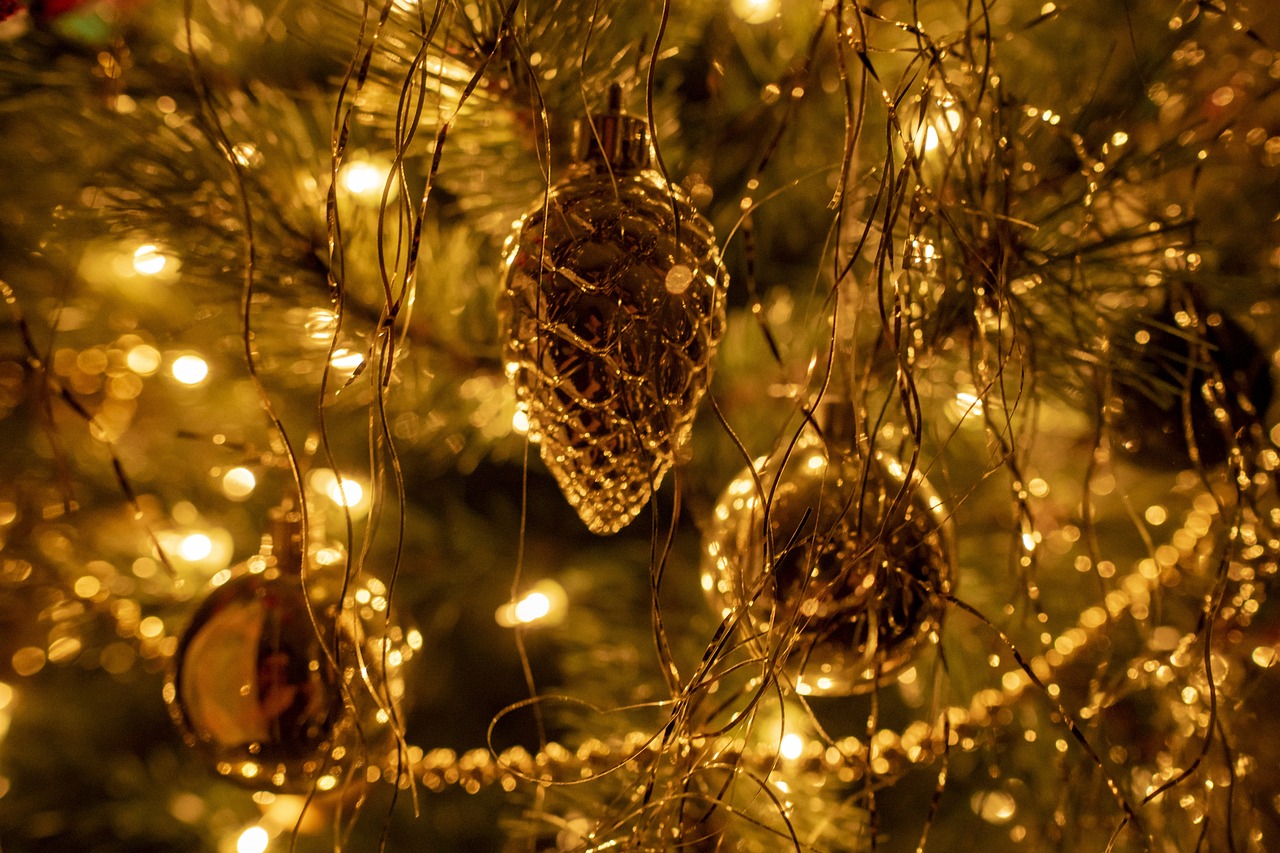 Close up photo of decorations hanging from a Christmas tree, they are all golden and lit up.