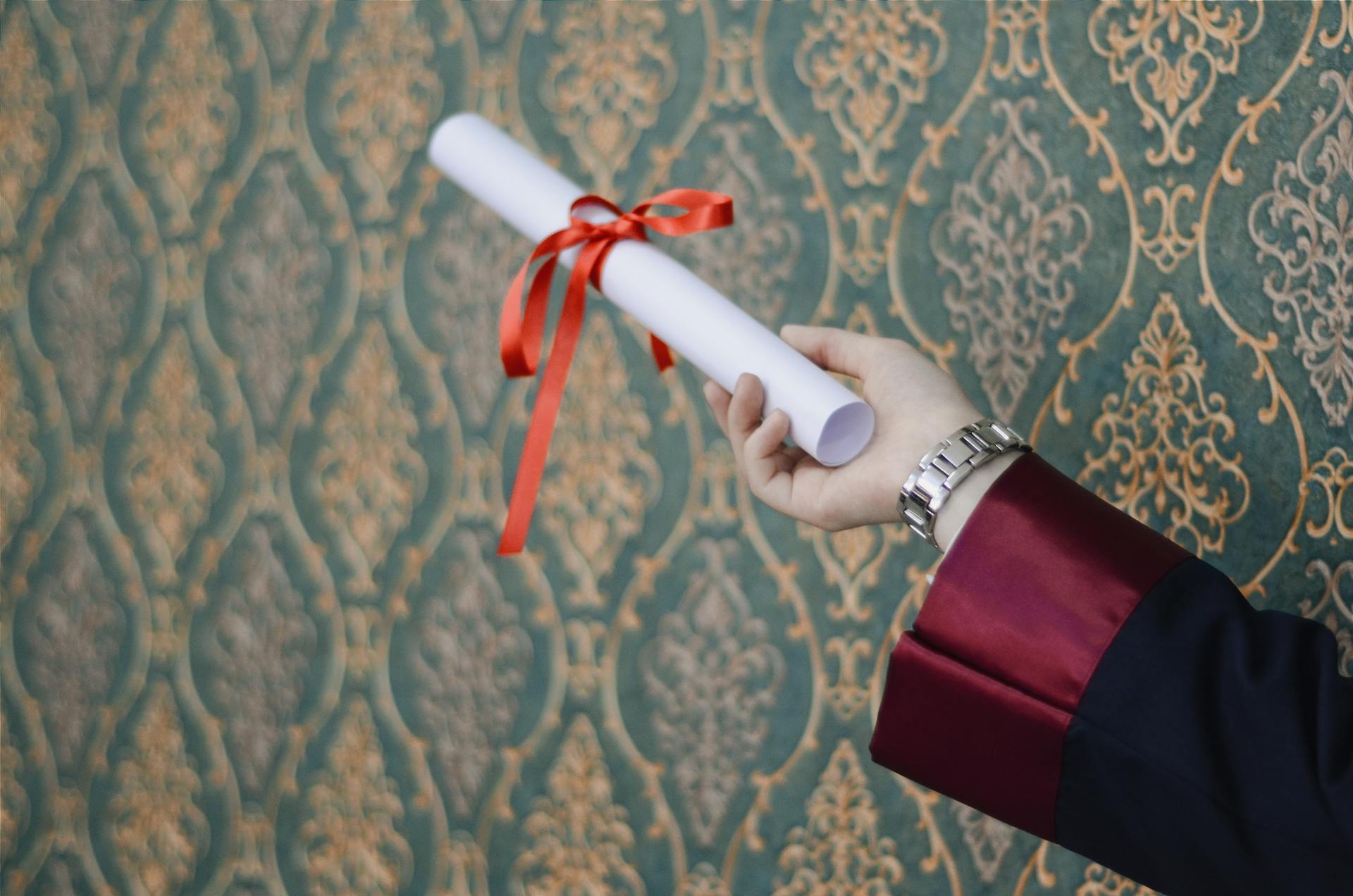 A hand holding a degree (with a red bow around it).
