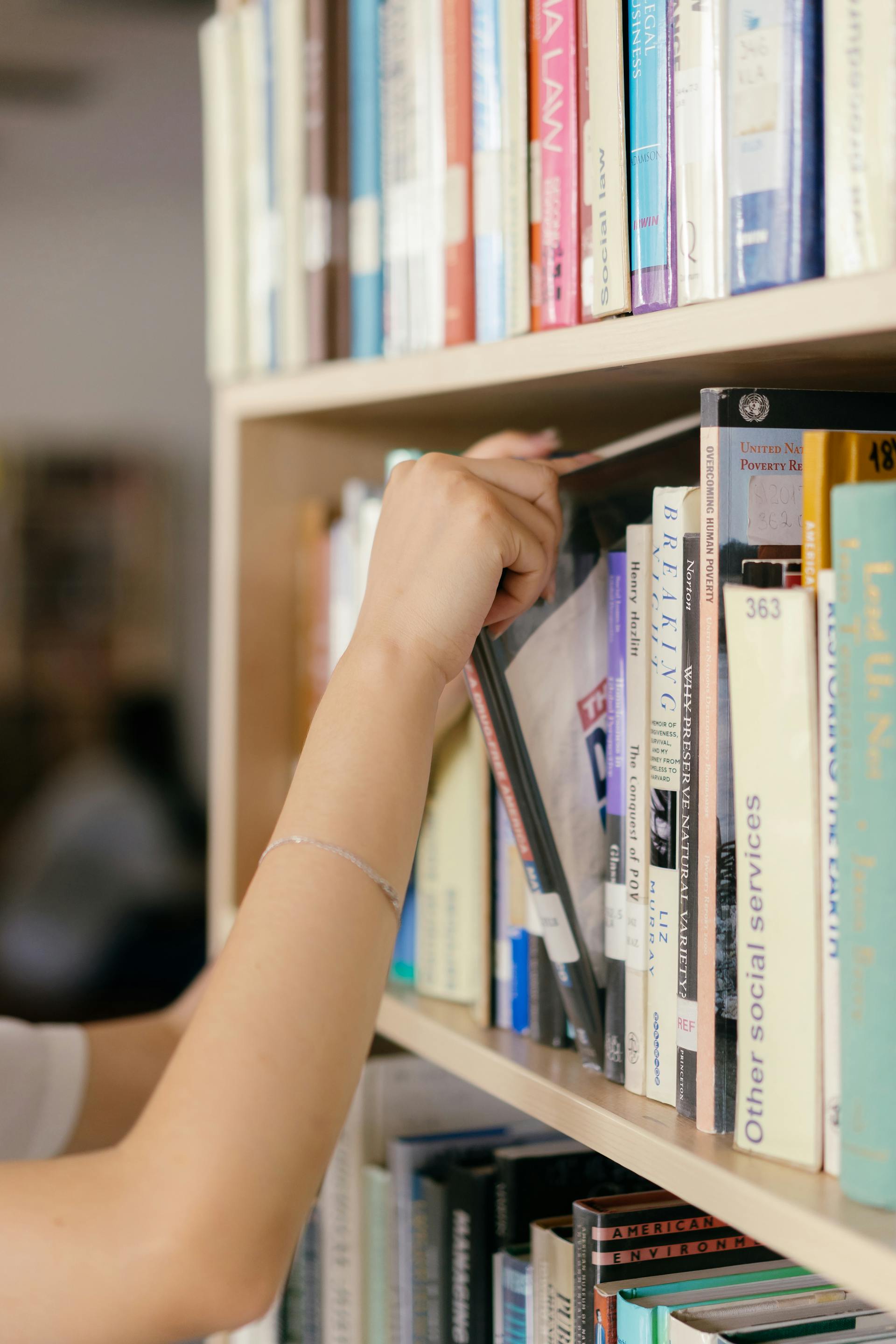 Someone choosing a book from a library shelf.