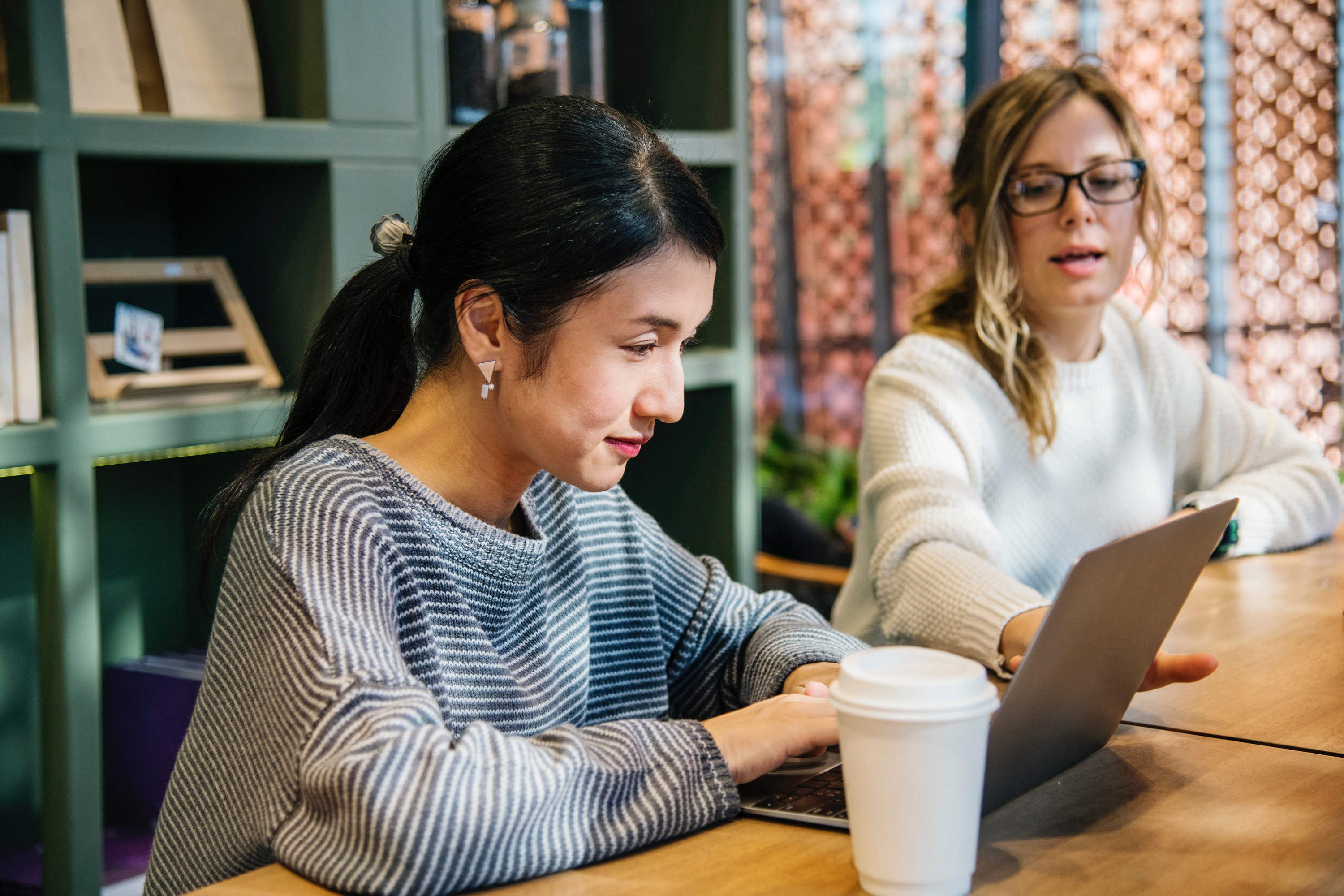 Two women sat at a desk, working on a laptop.