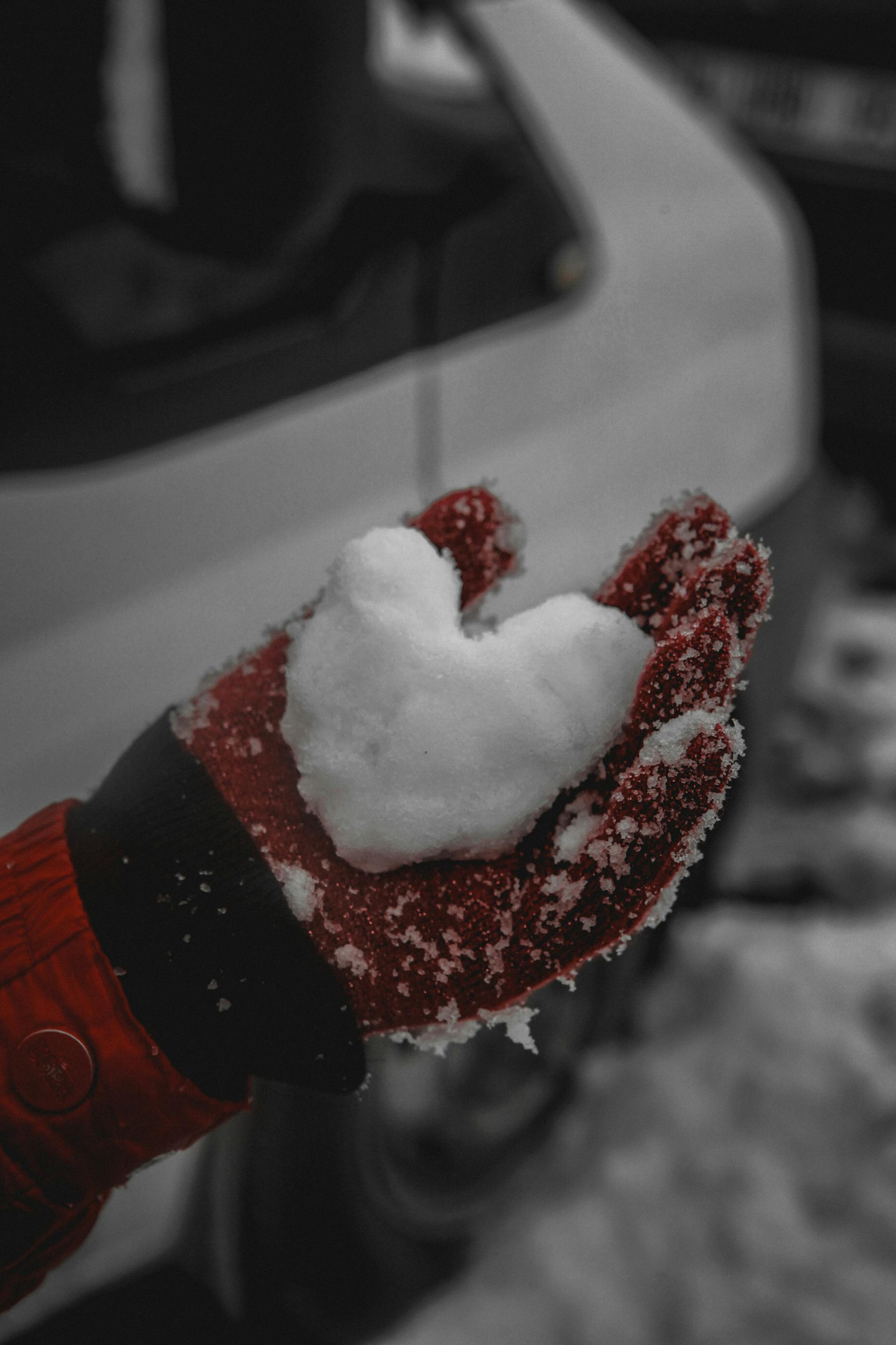 A glove holding a heart made out of snow.