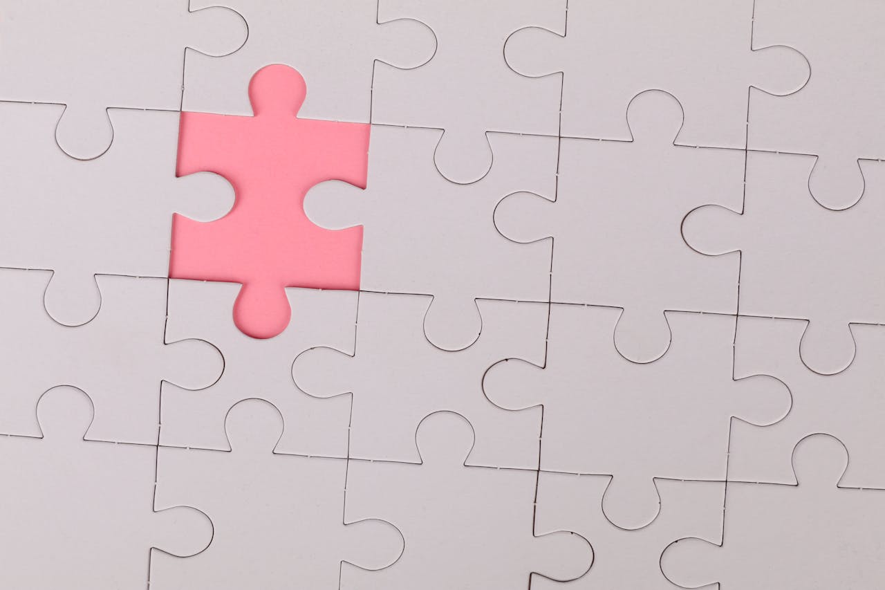 A white jigsaw puzzle with one pink piece.