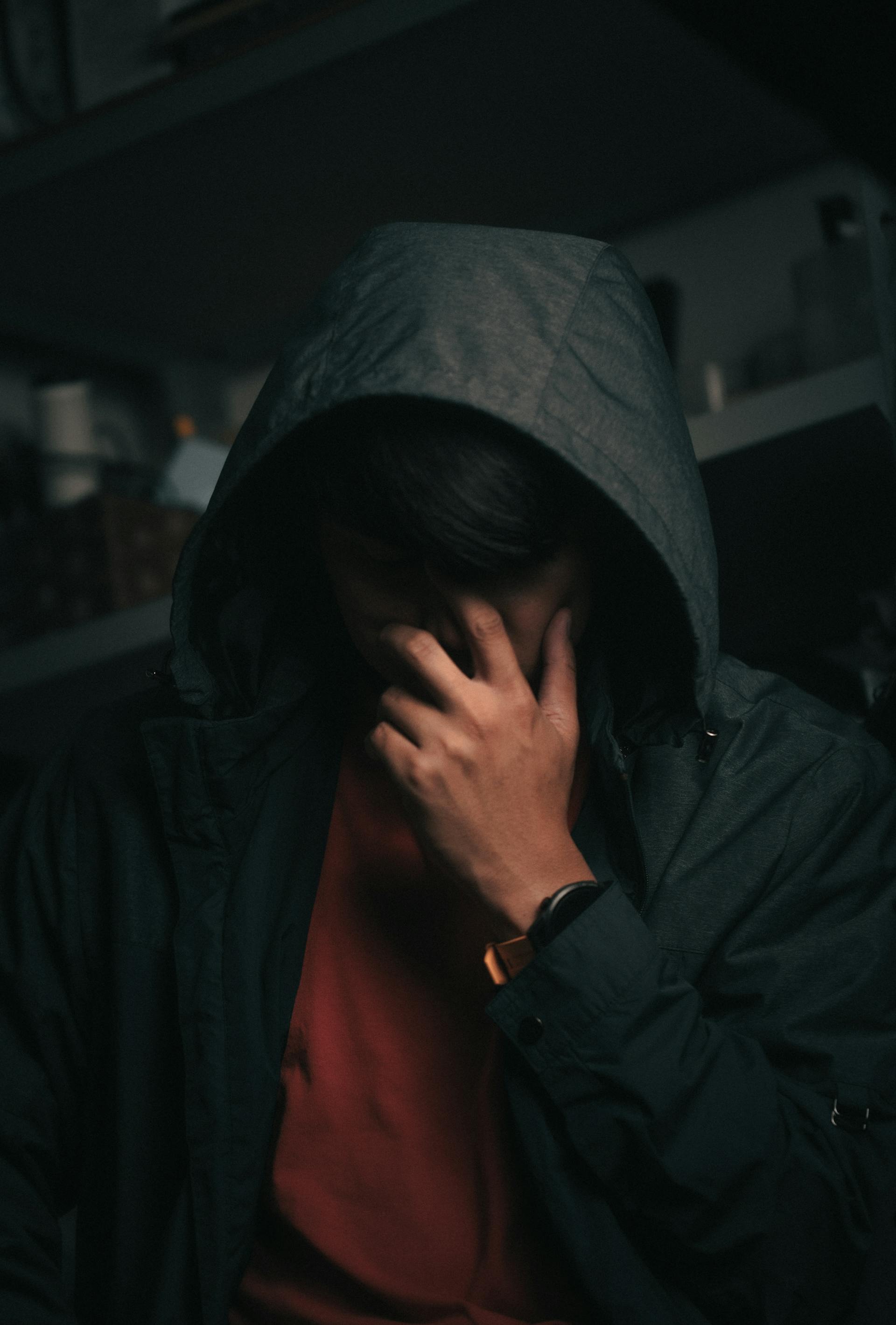 An anxious man in a hood, covering his face.